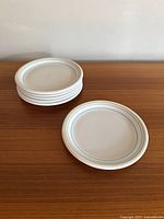 Six stacked white ceramic plates with blue and yellow rings on the rim, displayed on a wooden surface.