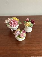 Three bone china flower bouquets arranged on a wooden surface showing frontal view with detailed flower shapes and colors.