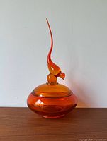 Front view of the vintage amber glass candy dish with decorative lid and finial on wooden surface against white wall.