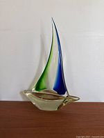 Full view of vintage glass sailboat figurine showing the yellow-tinted clear glass hull and green and blue tall sails.