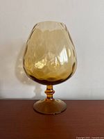 Amber-tinted vintage glass vase with hammered texture and scalloped rim, standing on a pedestal base, shown from side angle.
