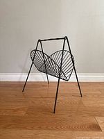 Front view of black metal wire magazine rack with wooden handle, showing curved, fan-like design and angled legs.