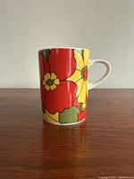 Side view of the vintage ceramic mug, showing vibrant red and yellow flower design with green leaves.
