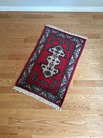 Top down view of vintage oriental rug with red and white geometric patterning and white fringe tassels at ends, placed on a hardwood floor.