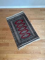 Full view of the small vintage area rug showing central three red diamond medallion pattern on dark background and fringed edges