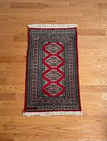 Top view of vintage rectangular rug with red central diamonds and intricate borders on hardwood floor.