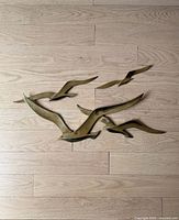 Five vintage brass seagull bird wall hangings arranged on a wooden floor showing overall shapes and layout.