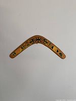 Top view of full wooden boomerang, showing curved shape and Aboriginal style art including frog and turtle motifs with red, yellow, and black paint on natural wood.