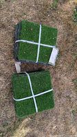 Two strapped bundles of artificial turf tiles on ground