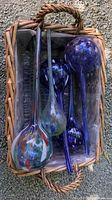Six glass watering globes of varying colours and patterns inside a wicker basket