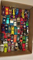 Top view of cardboard box containing roughly 40 Hot Wheels cars arranged in rows