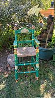 Front view of painted green folk art highchair in garden setting