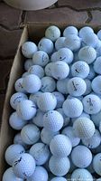 Top view of box filled with white golf balls showing various brand markings