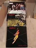 Stack of vinyl LP albums including Max Webster albums with colorful cover art, seen on carpet floor.