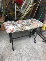 Full view of metal bench showing floral upholstery seat and ornate metal base with curved legs.