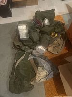 Assortment of canvas bags, pouches, canteen covers, bare canteen, mess tray and pan on concrete floor