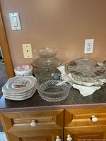 Overview of Johnson Bros ceramic plates in various pastel colors, clear glass pedestal cake plate, glass bowls and dishes set on kitchen counter.