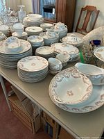 Full view of vintage china set on table showing plates, bowls, serving pieces, cups, and saucers with pink floral pattern and gold trim.
