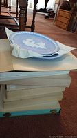 Stack of boxed collector plates with one plate on top wrapped in paper showing blue jasperware and white relief.
