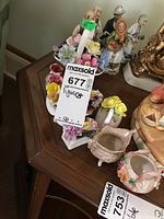 Wide view showing several Capodimonte style flower decorations and figurines arranged on a wooden surface, with price tags visible