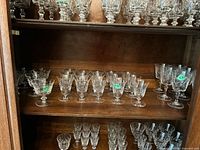 Set of cut crystal stemware glasses arranged on a wooden shelf, showing the variety of sizes and designs.