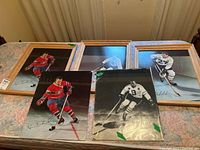 Five hockey prints arranged on a bed, three framed and two unframed prints visible, showing hockey players in vintage uniforms including the Montreal Canadiens and Toronto Maple Leafs.