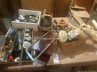 Wide shot of assortment of tools and hardware supplies including bow saw, baskets with small parts, hand tools, and containers.