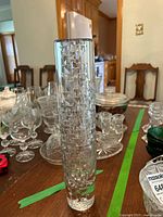 Front view of the tall clear vase with geometric faceted pattern on wooden table among other glass items