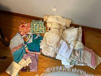 Grouped assorted vintage aprons, hand-crafted doilies, and linen napkins arranged on wooden floor showing general contents of the lot.