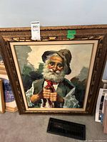 Frontal view of the full framed painting resting on floor, showing the elderly man with white beard, brown hat, and dark green vest with red necktie.