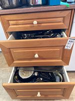 Two wooden kitchen drawers partially open showing various pots, pans and lids inside, items stacked within the drawers.