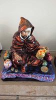 Front view of the Royal Doulton The Potter figurine showing the potter dressed in a brown hooded robe arranging colorful pottery on a textured base.