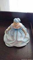 Top view of ceramic figurine showing the woman in a light blue dress with puffed sleeves and matching hat.