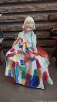 Front view of Royal Doulton figurine showing woman holding colorful patchwork quilt seated on orange armchair.
