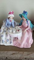 Front view of porcelain figurine showing two women seated at tea table