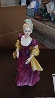 Front view of Royal Doulton figurine showing woman's face, purple dress and yellow shawl.