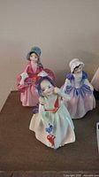 Photo showing three Royal Doulton porcelain figurines, front view, detailed close-up of faces and dresses.