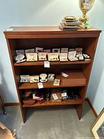 Front view of the wood veneer shelving unit with three shelves, empty except for items placed on and around it not included in lot.