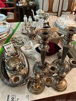 Photo showing six silver-plated candle holders of varying heights, creamer, sugar bowl, silver tray, and colored glass pieces on table.