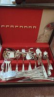 Full set of silver plated forks, knives, spoons organized in red fabric-lined case with utensil slots.