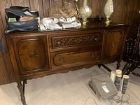 Front view of vintage wooden sideboard showing detailed center drawer carvings and side cabinet doors, with various unrelated items on top.