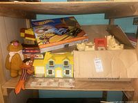 Photo showing Hot Wheels slot car track set box, Sesame Street plush toys, model house, Monopoly game box, and other boxes