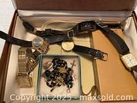 Open jewelry box displaying watches, pens and rosary/charm set