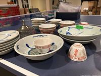 Various Asian-style bowls and cups arranged on a table, showing their size variation, patterns, and some chips.