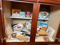 Full view of cabinet shelf showing assortment of baking items including cookie cutters, cooling racks, rolling pin, trivets, and baking cups.