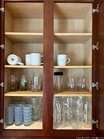 Full cabinet view showing all glassware stored inside wooden cabinet with glass doors.