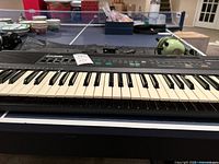 Casio CT-607 keyboard showing keys and front control panel with function buttons and sliders. Table tennis table visible in background.