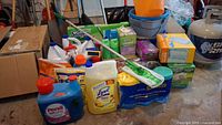 Wide shot showing whole lot of assorted cleaning supplies including detergents, sprays, Swiffer refills, sponges, buckets, and broom handle.