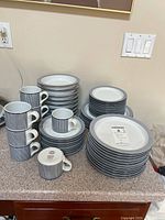 Photo showing stacks of mugs, dinner plates, smaller plates, and shallow bowls with blue patterning on countertop.