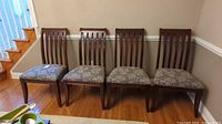 Four slat-back hardwood dining chairs lined up against wall with floral upholstered seats